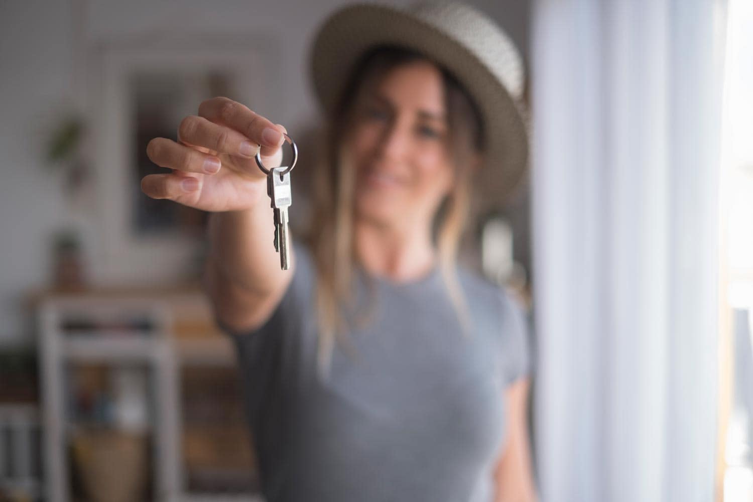 Vermietung: Junge Frau hält Wohnungsschlüssel in die Kamera